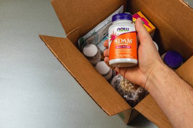 Lviv Ukrayna 10.04.25 Bir el, açık bir karton kutunun içinde çeşitli ek ürünlerle çevriliyken bir şişe multivitamin tutuyor..