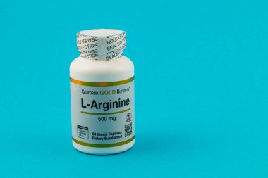 Lviv Ukrayna 10.04.25 Bir şişe L Arginine diyet takviyesi katı mavi arka planda sergilenmektedir. Etikette, ürünün her biri için 500 mg 'lık 60 sebze kapsülü içerdiği yazıyor..