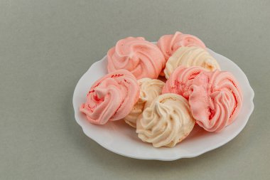 Pembe ve beyaz kurabiyelerden oluşan bir koleksiyon yuvarlak beyaz bir tabakta oturur ve tatlı aşıkları veya özel durumlar için mükemmel bir ziyafet sunar..