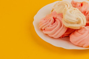 Pembe ve beyaz kurabiyelerden oluşan bir tabak, canlı sarı bir arka plana karşı enfes bir doku ve renk sunar..