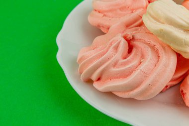 Pembe ve beyaz renkte yumuşak kremalar beyaz bir tabakta otururlar, parlak yeşil bir arka planla canlı bir tezat oluştururlar. Harika bir ikramdı.