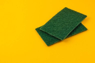 İki yeşil temizlik yastığı canlı sarı bir arka plana yerleştirilmiş. Ev temizlik işleri ve mutfak yüzeylerinin bakımı için mükemmel..