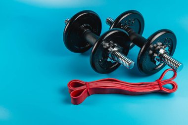 Siyah halterler, kırmızı direnç bantlarının yanına, parlak mavi bir yüzeye yerleştirilir. Bu da evde güç eğitimi için ideal bir fitness düzeneği sunar..
