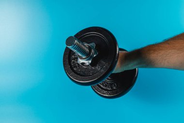 Bir insan tek eliyle siyah bir dambılı kaldırıyor, parlak mavi bir arka plana karşı, güç eğitimi ve fitness aktivitesi sergiliyor..