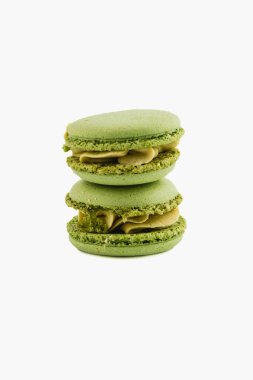 Üç yeşil badem kurabiyesi düzgünce istiflenmiş, hassas dokularını ve kremsi dolgularını sergiliyorlar. Canlı renkleri ve kusursuz şekilleri çekici bir tatlı gösterisi sunuyor..