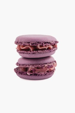 Pürüzsüz çikolata dolgulu iki mor badem kurabiyesi zarif bir şekilde istiflenir, zarif dokularını ve canlı renklerini düz bir arkaplanda sergilerler..