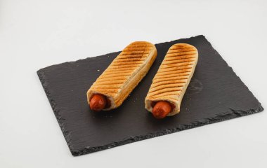 İki ızgara sosisli sandviç, kızarmış çöreğin içinde servis panosunun üzerinde. Lezzetli bir aperatif seçeneği sunuyorlar. Toplanma ya da günlük yemek için mükemmel..