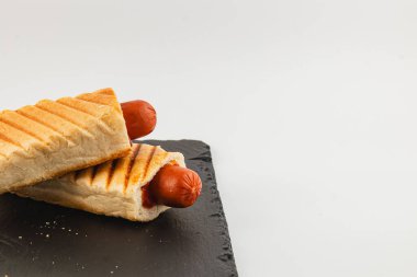 İki ızgara sosisli sandviç, kızarmış ekmek rulolarının içine koyuluyor, siyah bir tabakta dinleniyorlar, lezzetli ve iştah açıcı bir aperatif sergiliyorlar..