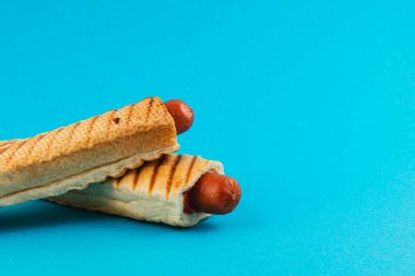 Kızarmış sosisli sandviçler, kıtır kıtır ekmeğin içine yerleştirilir. Parlak mavi bir arka plana karşı güzelce düzenlenir. Eğlenceli ve iştah açıcı bir mutfak yaratımı sergiler..