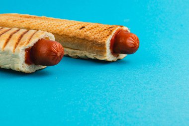 İki ızgara sosisli, parlak mavi bir yüzeyde waffle ekmeğinin içine yerleştirilir. Bu kombinasyon klasik sokak yemeklerinde yaratıcı bir değişiklik sağlıyor..