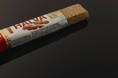 Lviv Ukrayna 05.06.25 Halva tatlı barı karanlık bir tabakta duruyor. Ürün, arka planda çarpıcı bir karşıtlık oluşturarak dokusunu ve malzemelerini sergiliyor..