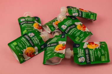 Lviv Ukrayna 05.06.25 organik mango kesesi ve şeftalili meyve püresi pembe arka planda, canlı ambalajlar ve çocuklar için sağlıklı atıştırmalıklar sergilenmektedir..