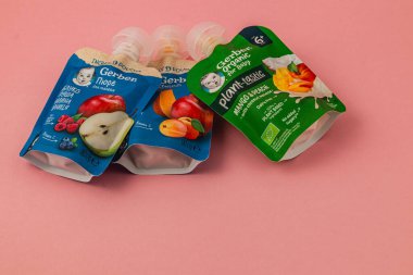 Lviv Ukrayna 05.06.25 Üç organik bebek maması kesesinde çeşitli meyve aromaları ve malzemeler bulunur. Renkli ambalajları yumuşak pembe bir arka plana karşı duruyor..