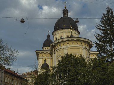 Lviv Ukrayna 04.18.25 Büyüleyici bir kilisede süslü kubbeler ve bereketli ağaçlarla çevrili altın haçlar ve bulutlu bir günde kentsel bir zemin bulunur. Barışçıl bir atmosfer hakim.