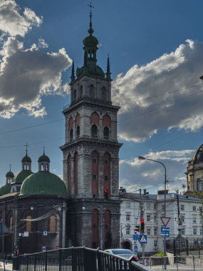 Lviv Ukrayna 04.20.25 Yeşil kubbeler ve şehir binalarıyla çevrili yüksek tarihi bir kule, bulutlar öğleden sonra gökyüzünde süzülürken.