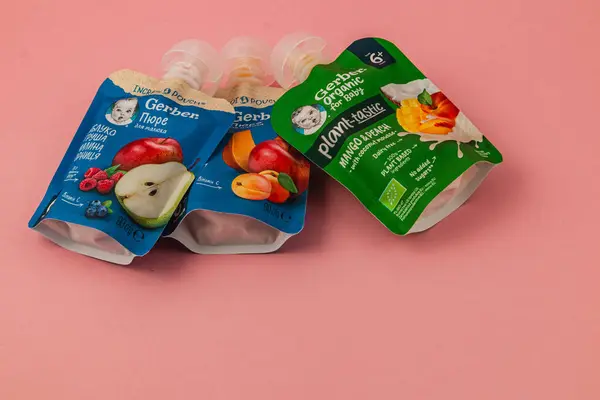 Lviv Ukrayna 05.06.25 Üç organik bebek maması kesesinde çeşitli meyve aromaları ve malzemeler bulunur. Renkli ambalajları yumuşak pembe bir arka plana karşı duruyor..