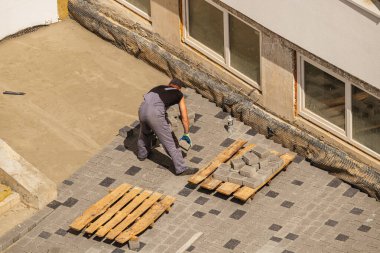 Lviv Ukrayna 04.30.25 Bir işçi inşaat sahasına kaldırım taşları bırakıyor. Gündüz aktivitesi, bir binanın etrafındaki hazırlanmış bir yüzeye düzenli olarak taş yerleştirmeyi içerir..