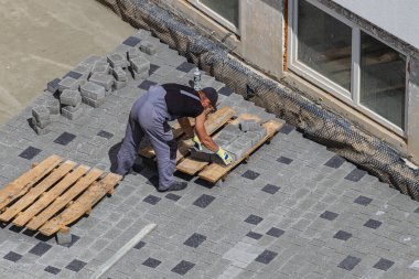 Lviv Ukrayna 04.30.25 İşçi, bu süreçte hareket kolaylığı için ahşap bir palet kullanırken, kesin bir hizalama sağlamak için, bir çatıdaki kaldırımları dikkatlice yerleştirir..