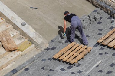 Lviv Ukrayna 04.30.25 Bir inşaat işçisi inşaat sahasına kaldırım taşlarını dikkatlice yerleştiriyor. Tahta paletler bölgede dinleniyor. Bu da devam eden faaliyetleri gösteriyor..