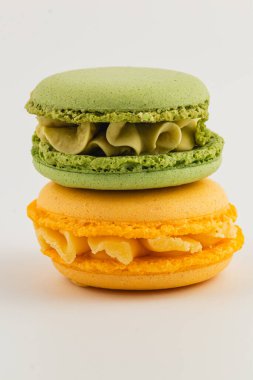 İki badem kurabiyesi ustalıkla istiflenmiş, biri kremalı canlı yeşil, diğeri de zengin dolgulu parlak sarı, lezzetli hamur işi sanatları sergiliyor..