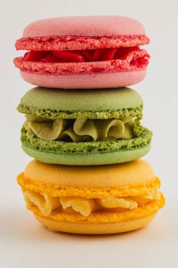 Üç canlı badem kurabiyesi güzel bir şekilde istiflenmiş, farklı renk ve dokularını sergiliyorlar. Bu güzel görüntü pembe, yeşil ve sarı ikramları vurguluyor..