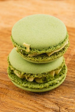 İki yeşil kibrit makaronu ahşap bir yüzeye istiflenmiş, desenli kabukları ve kremalı dolgusu sergileniyor. Doğal ışık altında çok güzel sunuluyorlar..