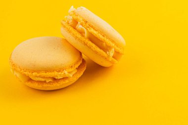 Kremalı kremayla dolu iki sarı badem kurabiyesi parlak sarı bir yüzeye yerleştirilmiş pürüzsüz dokularını ve çekici renklerini sergiliyorlar..