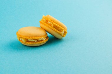 Kremayla dolu iki lezzetli sarı badem kurabiyesi parlak mavi bir yüzeye karşı şakacı bir şekilde oturur. Yumuşak dokular ve canlı renkler cezbedici bir ziyafet yaratır..