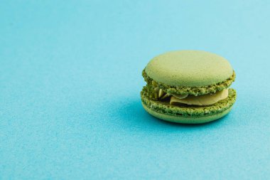 Narin yeşil bir makaron canlı mavi bir yüzeye dayanır, pürüzsüz dokusunu ve katmanlı dolgusunu sergiler. Kompozisyon tatlının detaylarını ve renk kontrastını vurguluyor.