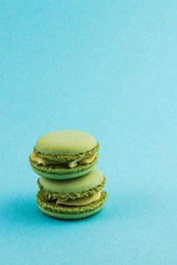 Kremayla dolu üç yeşil badem kurabiyesi parlak mavi bir arka fona karşı istiflenmiş ve desen ve renklerini sergiliyorlar. Tatlı severler için enfes bir ikram..