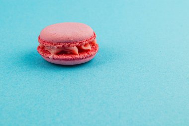 Tek bir pembe badem kurabiyesi parlak mavi bir yüzeyde zarif bir şekilde durur. Tatlandırıcı yumuşak bir krema içeriyor ve hafif, havadar bir dokusu var, tatlı çekiciliğini gösteriyor..