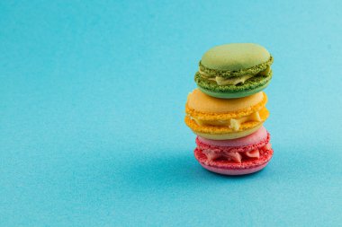 Canlı renklerde dört badem kurabiyesi yığını mavi bir yüzeye dayanır. Tadı değişik, gösterişli yeşil, sarı, pembe ve turuncu renkler, hoş görünümlerini vurguluyor..