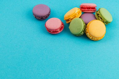Değişik aromalı parlak renkli badem kurabiyeleri canlı mavi bir yüzeyde sergileniyor. Tatlıları ve toplantıları sevenler için mükemmel bir davet sunuyor..