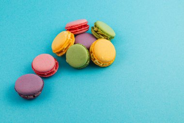 Çeşitli renklerde birkaç canlı badem kurabiyesi pürüzsüz, parlak mavi bir zemin üzerinde oturur ve narin dokularını ve eşsiz lezzetlerini sergiler..