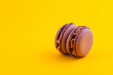 Parlak sarı bir yüzeyde dinlenen iki çikolatalı kurabiye pürüzsüz dokularını ve dolgusunu sergiliyor. Arkaplandaki karşıtlık onların detaylarını vurgular.