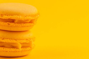 İki canlı sarı badem kurabiyesi, neşeli sarı bir zemin üzerinde duruyor, pürüzsüz dokularını ve kremsi dolgularını sergiliyorlar, tatlı için mükemmel..