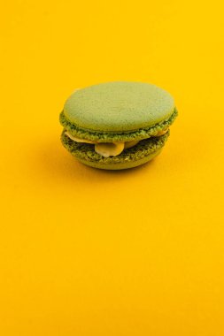 Yeşil bir badem kurabiyesi canlı sarı bir zemin üzerinde oturur. Karmaşık tasarımı ve dokusunu sergiler. Tatlı şekerlemeler mutfağın yaratıcılığını ön plana çıkarıyor..