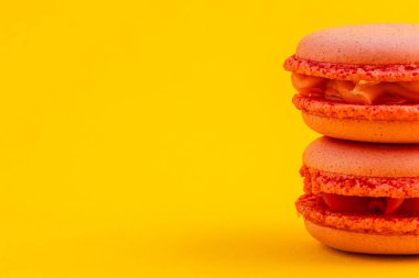 İki canlı turuncu badem kurabiyesi birbirinin üzerinde dinleniyor, zarif dokularını ve kremsi dokularını neşeli sarı bir arka plana sergiliyorlar..