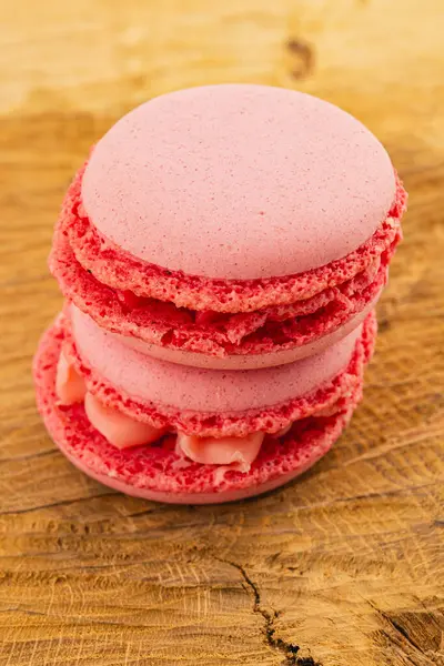 İki canlı pembe badem kurabiyesi düzgün bir şekilde ahşap bir masaya istiflenir. Narin dokuları ve kremalı dolguları davetkar bir tatlı gösterisi yaratıyor..