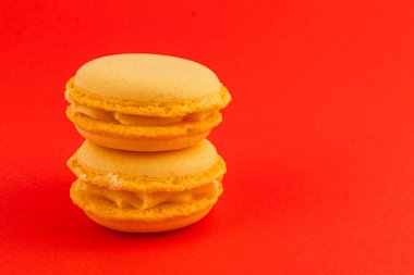 Kremayla dolu iki sarı badem kurabiyesi parlak kırmızı bir zemin üzerinde üst üste istiflenerek pürüzsüz dokularını ve canlı renklerini sergiliyorlar..