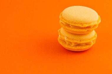 Kremalı iki lezzetli turuncu badem kurabiyesi parlak turuncu bir zemin üzerine istiflenmiş, dokularını ve renklerini mükemmel bir şekilde renklendiriyorlar..