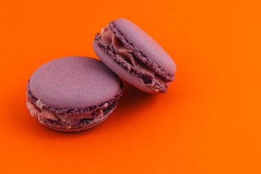 Çikolatalı ganache ile dolu iki lezzetli mor badem kurabiyesi parlak turuncu bir arka planda oturur, tatlı sevenler ve pasta sevenler için çekicidir..