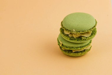 Yumuşak turuncu bir zemine karşı üst üste yığılmış üç canlı yeşil badem kurabiyesi pürüzsüz dokusunu ve zarafetini ön plana çıkarıyor..