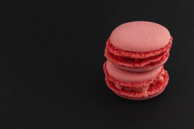 Pembe badem kurabiyeleri koyu bir arka planda çekici bir şekilde istiflenir, pürüzsüz dokularını ve canlı renklerini sergilerler, tatlı severler ve özel durumlar için mükemmeldirler..