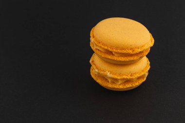 Kremayla dolu iki canlı sarı badem kurabiyesi karanlık bir yüzeyde oturup pürüzsüz dokularını ve tatlı aşıkları için davetkar görünüşlerini sergiliyorlar..