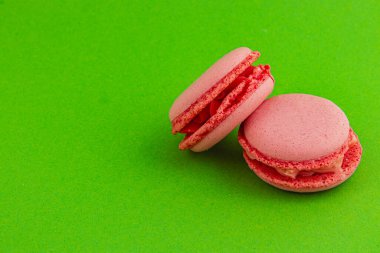 Pembe badem kurabiyeleri parlak yeşil bir zemine yaslanmış, pürüzsüz, yuvarlak kenarlarını ve kremsi dokularını sergiliyorlar, tatlılıklarını ve dokularını vurguluyorlar..