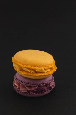 İki badem kurabiyesi ustalıkla istiflenmiştir, üstünde parlak sarı bir tane, altında da zengin mor bir tane vardır, enfes dokularını ve renklerini sergilerler..