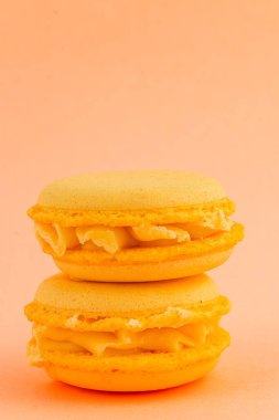 İki sarı badem kurabiyesi yumuşak pastel arka planda yan yana dizilmiş. Narin kurabiyelerin kremalı dolgusu ve canlı bir rengi var..