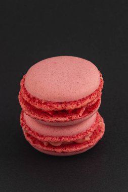 İki kırmızı badem kurabiyesi düzgün bir şekilde koyu bir arkaplana karşı istiflenir, pürüzsüz dış ve hassas dolgularını sergilerler, cazip bir tatlı gösterisi yaratırlar..