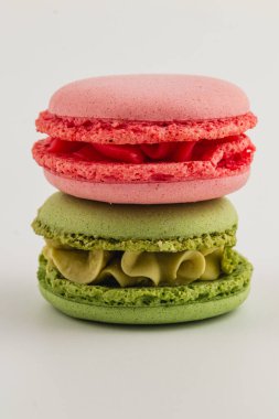 İki canlı badem kurabiyesi, biri pembe ve biri yeşil, sanatsal olarak temiz beyaz bir yüzeye istiflenmiş, hassas dokularını ve parlak renklerini sergiliyorlar..